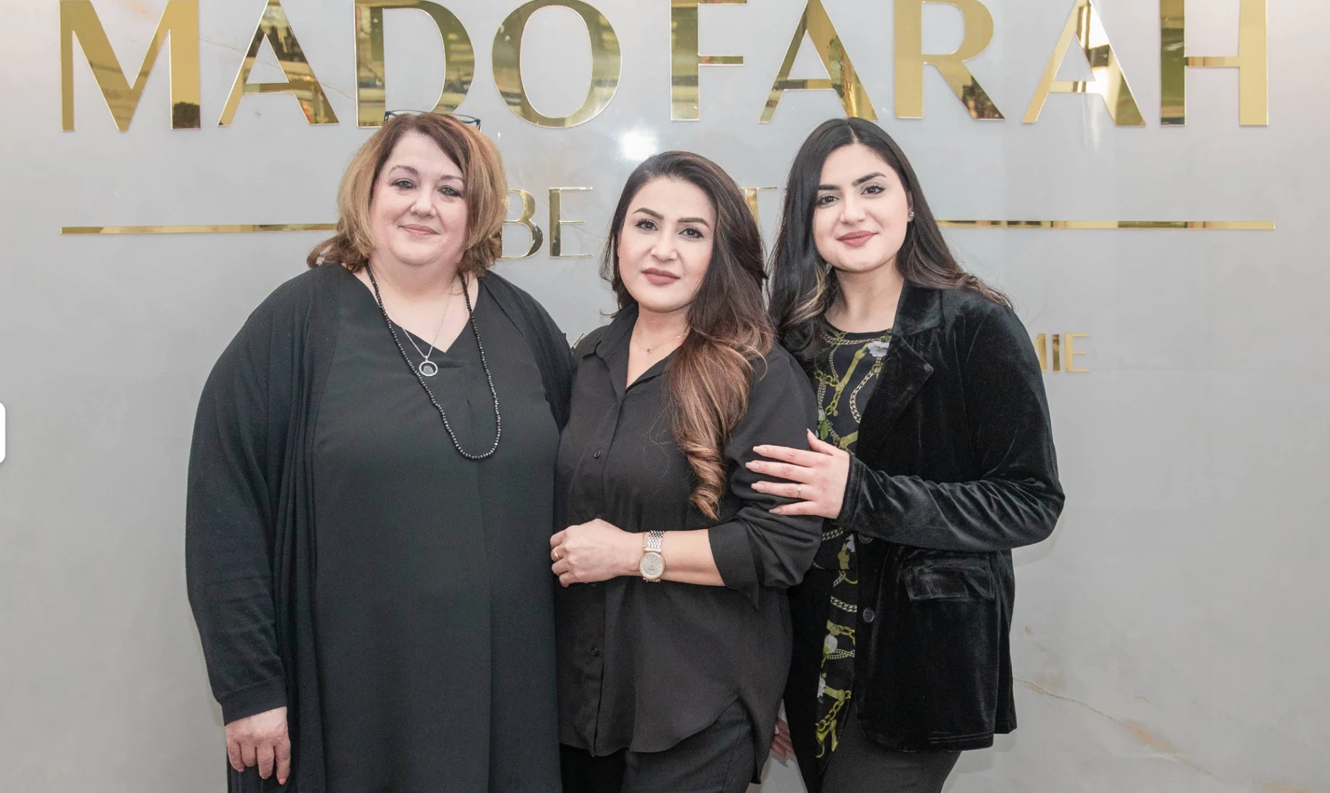 Drei Mitarbeiterinnen von MadoFarah Beauty in Schwarz vor dem goldenen Schriftzug des Salons.