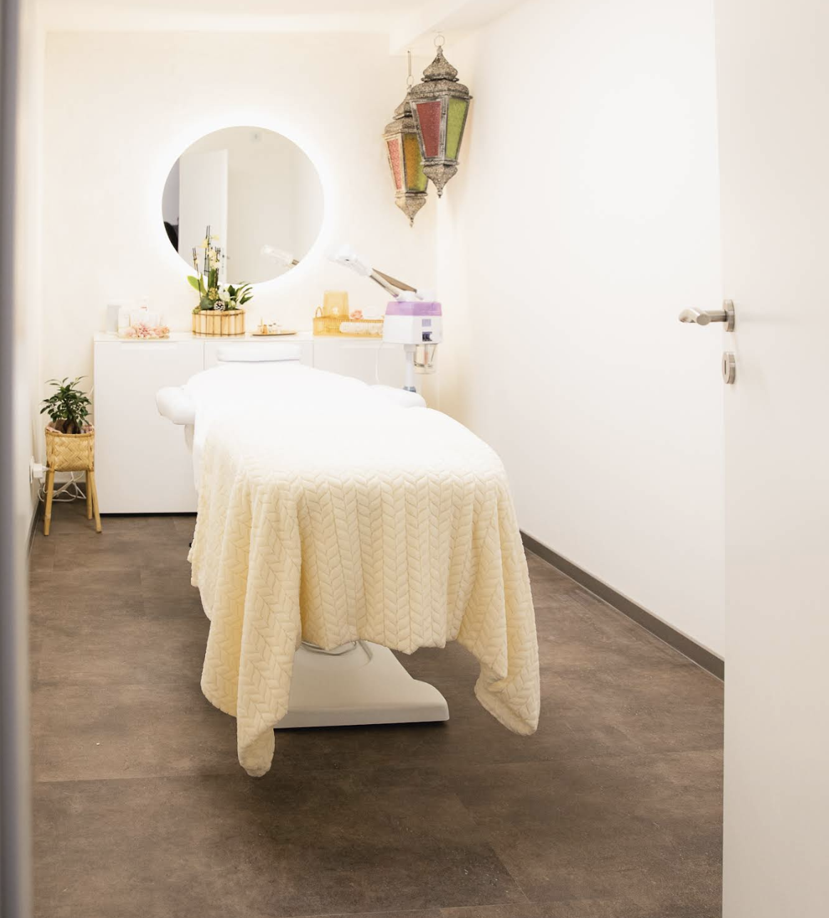 Kosmetikkabine bei MadoFarah Beauty mit Behandlungsliege, runder Spiegelleuchte und Pflegeprodukten.